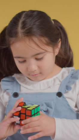 Vertical-Video-Studio-Close-Up-Of-Young-Girl-On-ASD-Spectrum-Solving-Puzzle-Cube-On-Yellow-Background